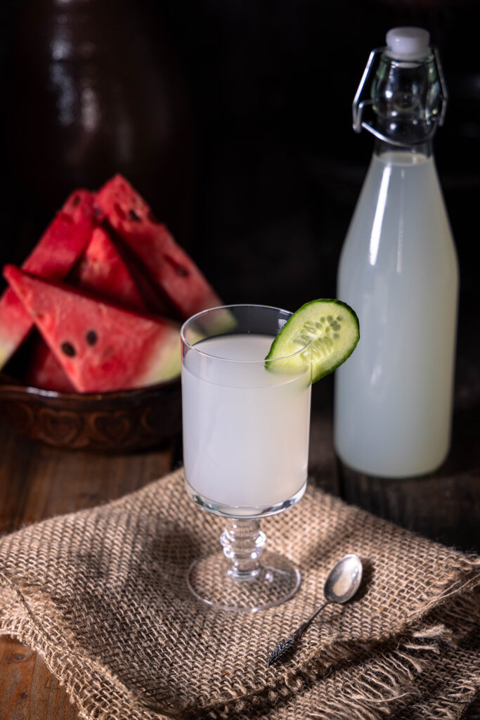 Ingwer-Bitterlemon-Kefir - in einem Glas und in einer Flasche. Außerdem eine Schale mit Melonenstücken.