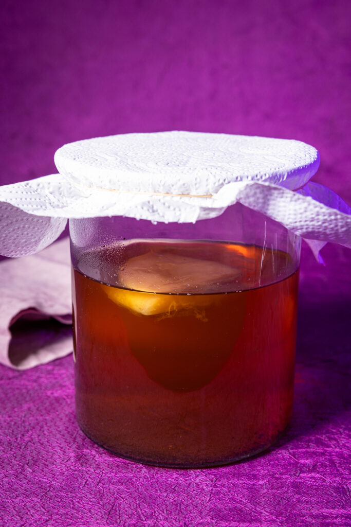 Ein Glasgefäß mit Kombucha, abgedeckt mit Küchenpapier.