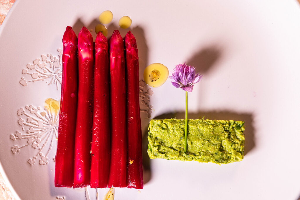 Pinker Spargelsalat in Form von 5 pinken Spargelspitzen, Schnittlauchhummus und Schnittlauchblüte mit Dressing auf einem Teller