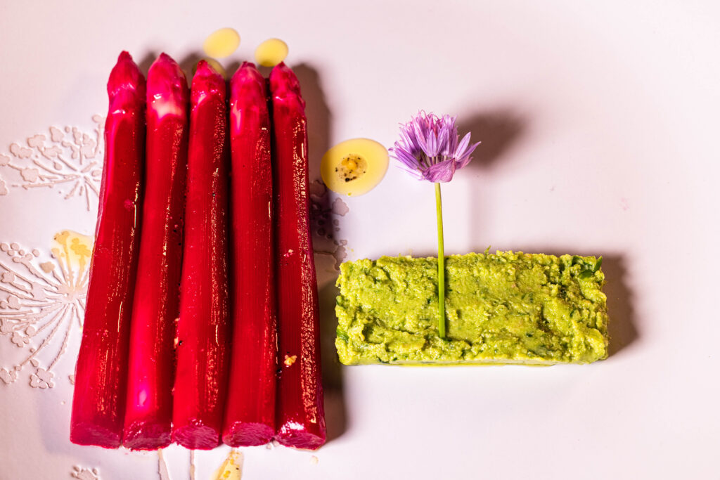 Pinker Spargelsalat in Form von 5 pinken Spargelspitzen, Schnittlauchhummus und Schnittlauchblüte auf einem Teller.