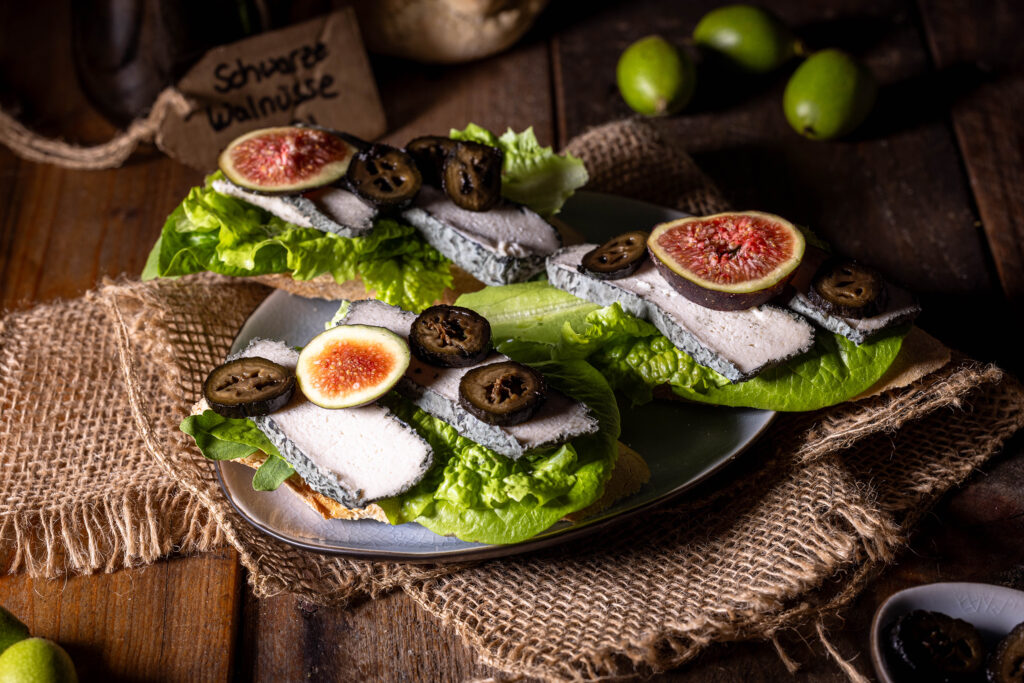 Schwarze Nüsse - eine Delikatesse aus grünen Walnüssen - hier mit Feigen auf veganem Blauschimmelkäse zu sehen.