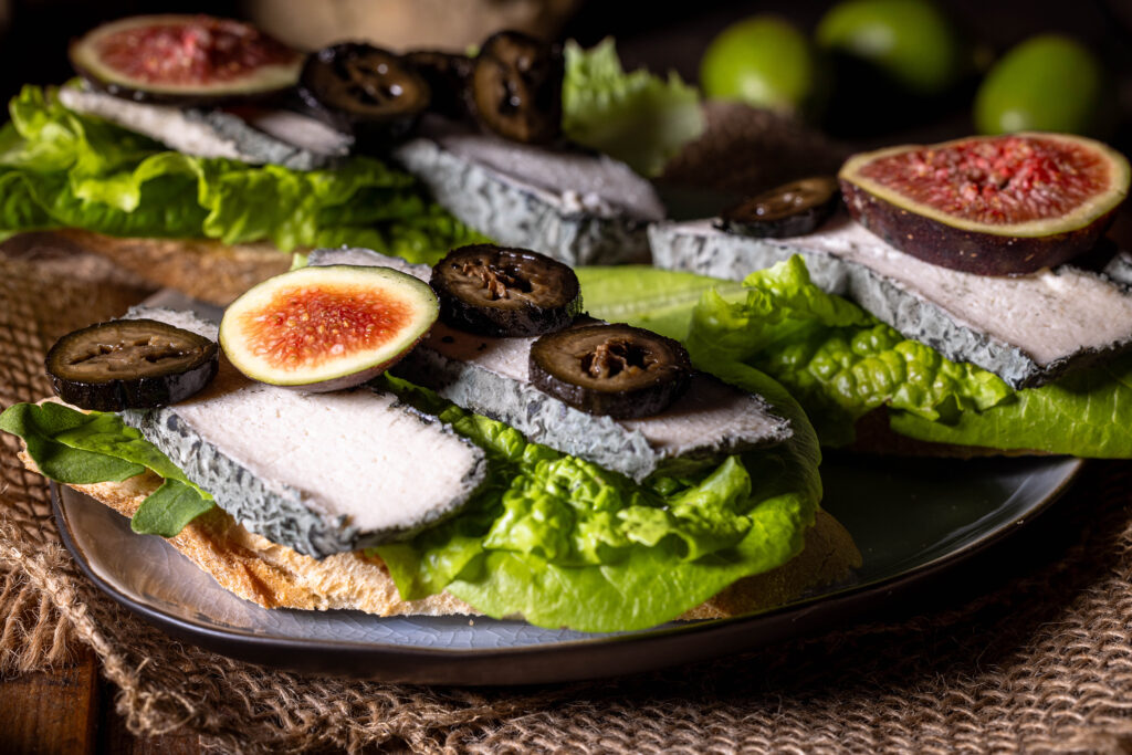 Schwarze Nüsse - eine Delikatesse aus grünen Walnüssen - hier mit Feigen auf veganem Blauschimmelkäse zu sehen.