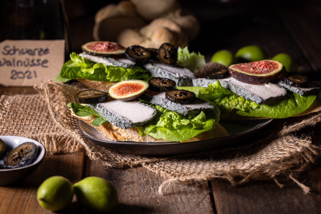 Schwarze Nüsse - eine Delikatesse aus grünen Walnüssen - hier mit Feigen auf veganem Blauschimmelkäse zu sehen.