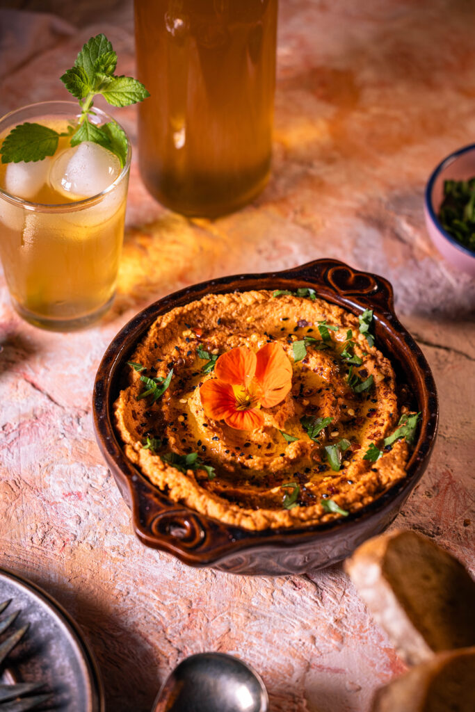 Tomaten-Hummus in einer Schale auf einem rötlichen Tisch.
