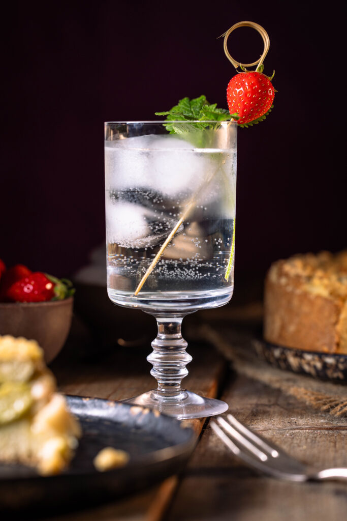 Ein Glas gefüllt mit Limonade aus Zitronenmelisse-Sirup und Eiswürfeln. Garniert mit frischer Zitronenmelisse und einer Erdbeere.