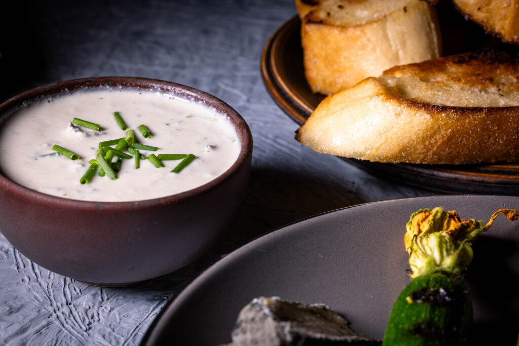 Veganer Blauschimmelkäsedip– in einer Schale, daneben ein Teller mit gerösteten Babyzucchini und ein Teller mit geröstetem Brot.