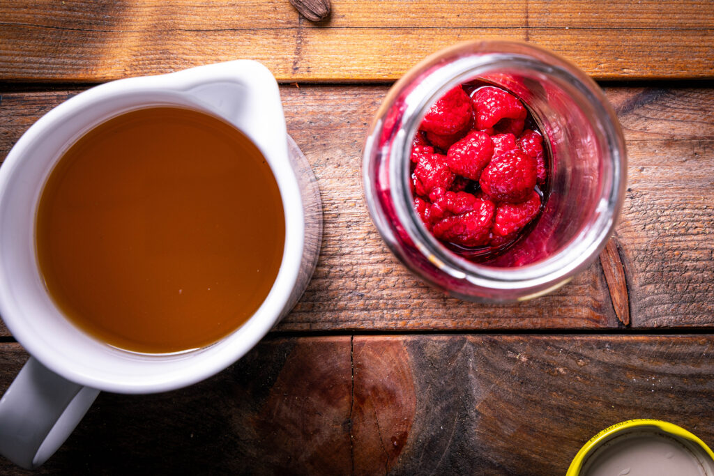 Eine Karaffe mit Kombucha und ein Glas mit Ahornsirup und Himbeeren darin.