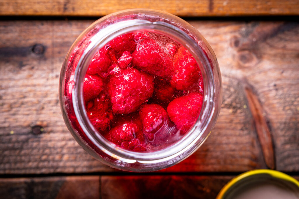 Ein Glas mit Kombucha, Ahornsirup und Himbeeren darin.