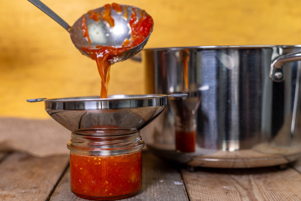 Tomatenmarmelade wird in ein Schraubglas gefüllt. Mit einer Kelle und einem Trichter.