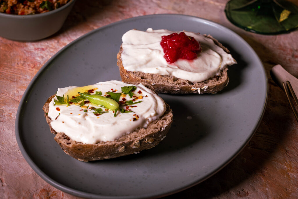 Vrischkäse - veganer Frischkäse auf Kefirbasis, auf zwei Brötchenhälften, eine mit Kräutern, eine mit Marmelade.