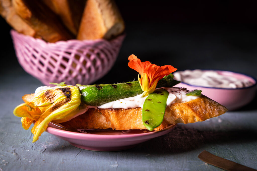 Veganer Frischkäse auf Kefirbasis mit geröstetem Gemüse und Kapuzinerkresse auf einem Stück Brot.