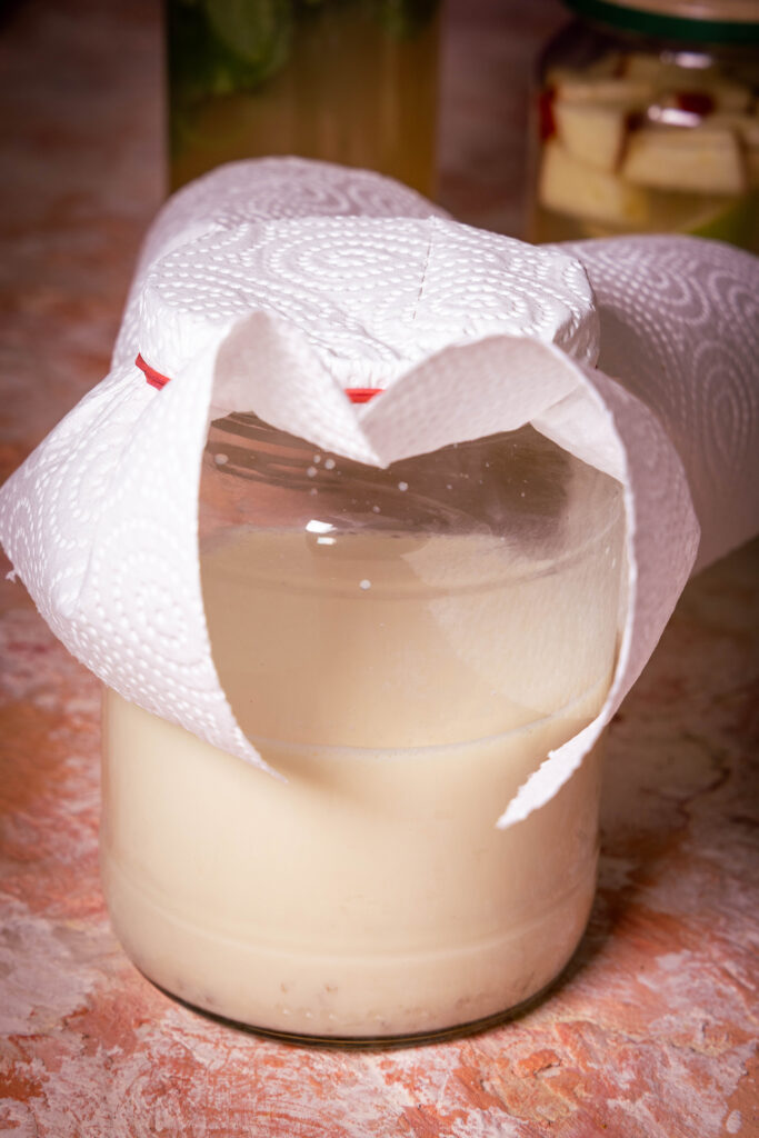 Ein Glas mit Sojamilch, abgedeckt mit einem Küchentuch.