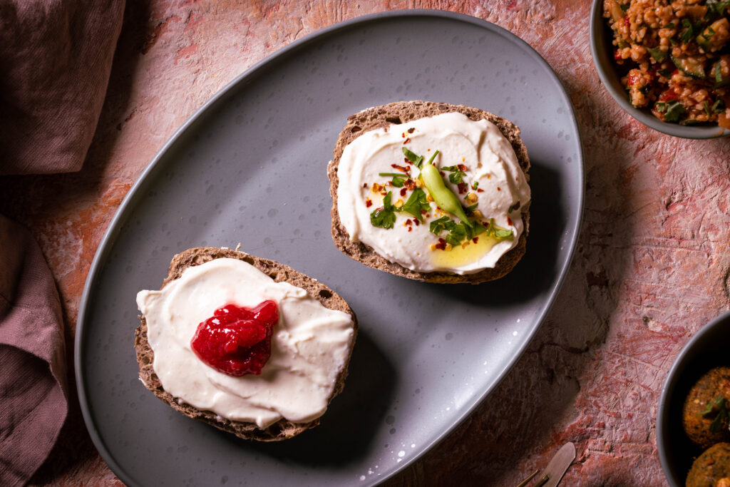 Vrischkäse - veganer Frischkäse auf Kefirbasis, auf zwei Brötchenhälften, eine mit Kräutern, eine mit Marmelade.