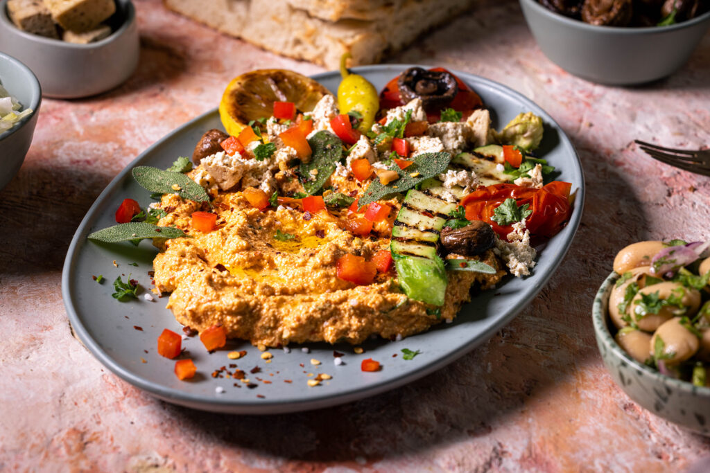 Veganer Scharfer Schafskäse Dip - Hot Sheperd - mit verschiedenen Beilagen auf einem Teller angerichtet.