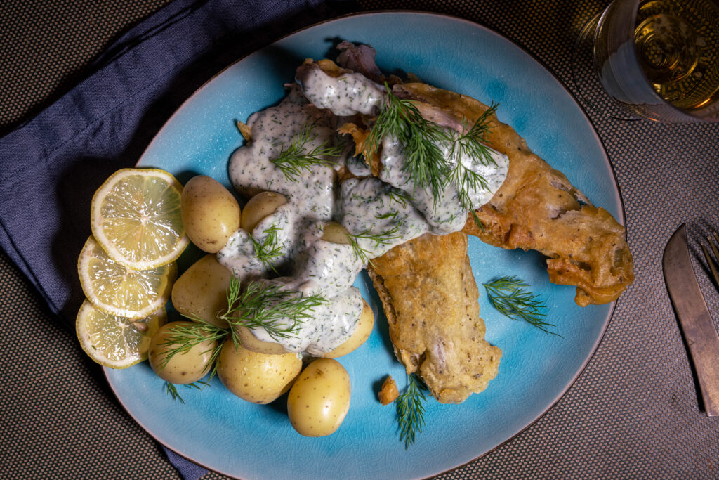 Visch, veganer Fisch, mit Dillsauce, Zitronenscheiben und Pellkartoffeln auf einem blauen Teller.