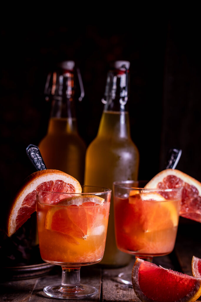 Grapefruit-Kombucha -in Gläsern mit Eis und frischer Grapefruit. Dahinter Kombucha in Flaschen.
