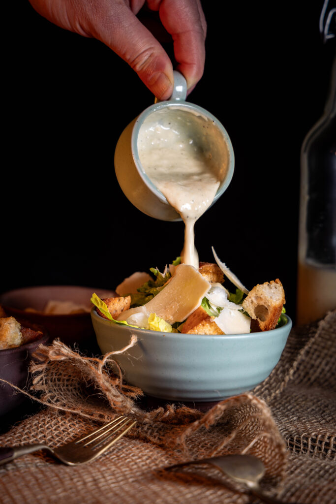 Veganes Caesar Dressing wird auf eine Salatschale gegeben.