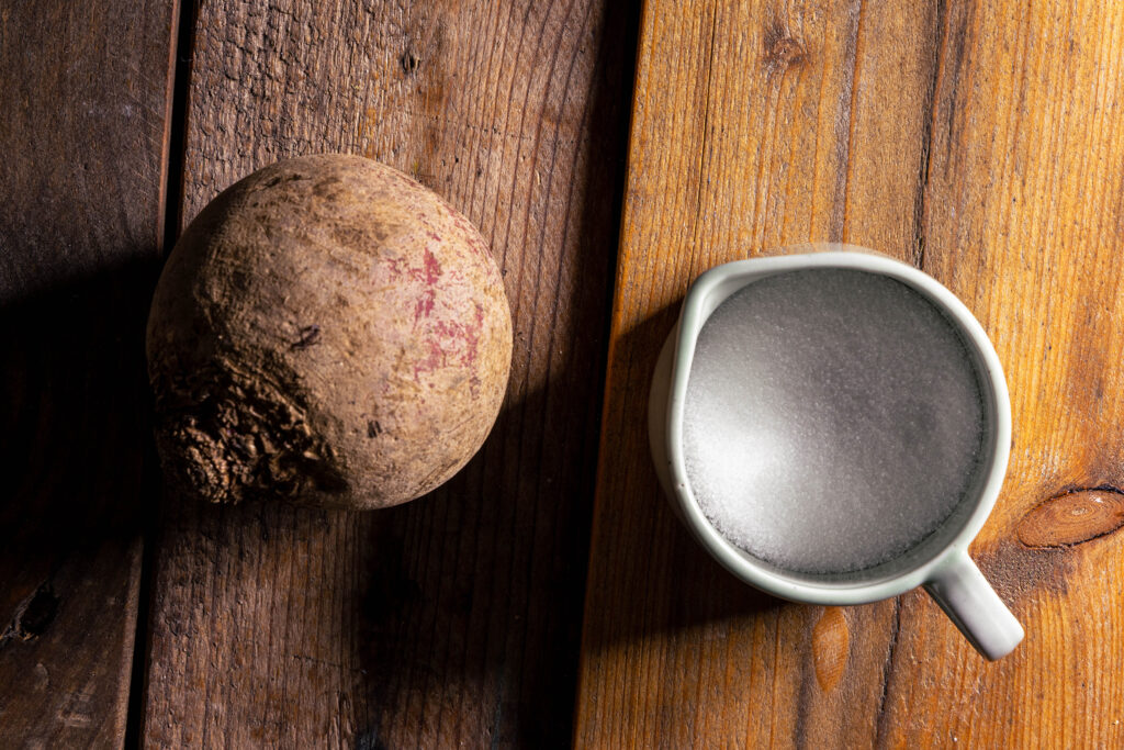 Eine Rote Beete und ein Schälchen Zucker auf einem Holztisch.