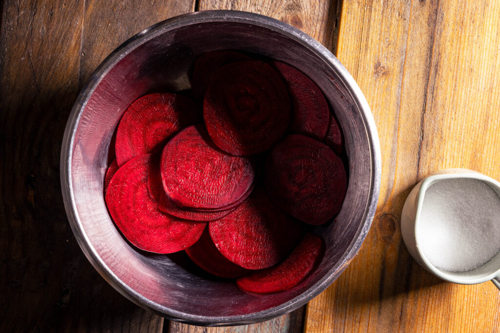 Gehobelte Rote Beete in einer Schüssel, daneben eine Schale Zucker.