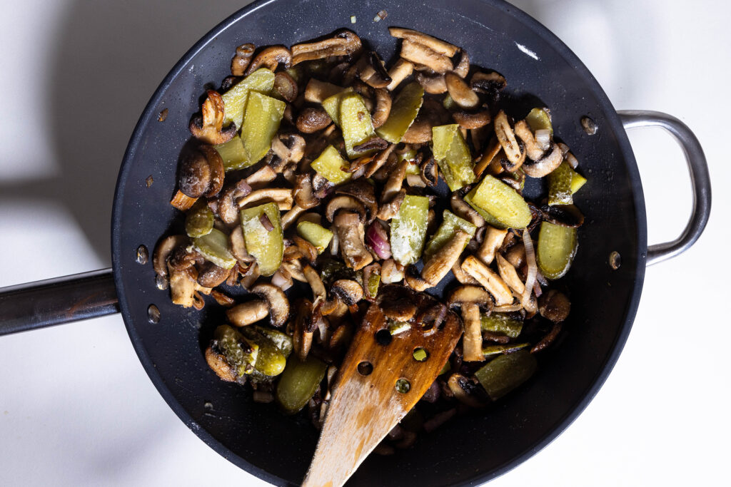 Schalotten, Champignons und Saure Gurken braten in einer Pfanne.