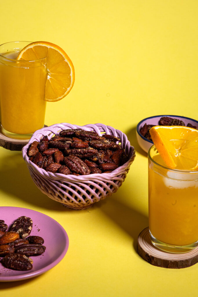 Orangen-Nüsse, in Schälchen auf gelbem Grund. Außerdem 2 Gläser Orangensaft.