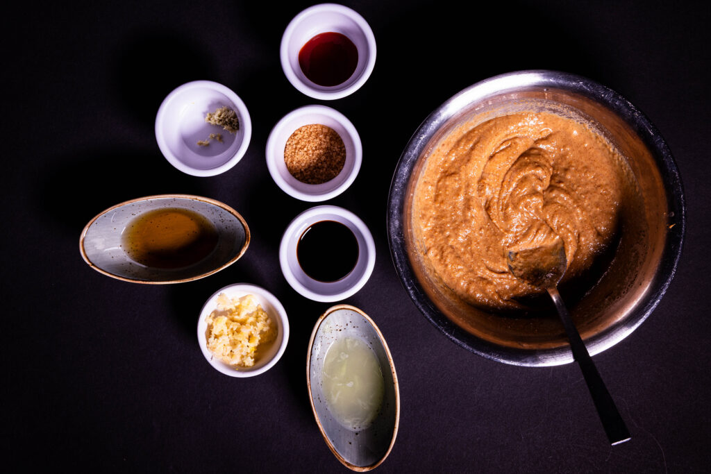 Erdnussbutter wird mit heißem Wasser verrührt. Daneben weitere Dressingzutaten.