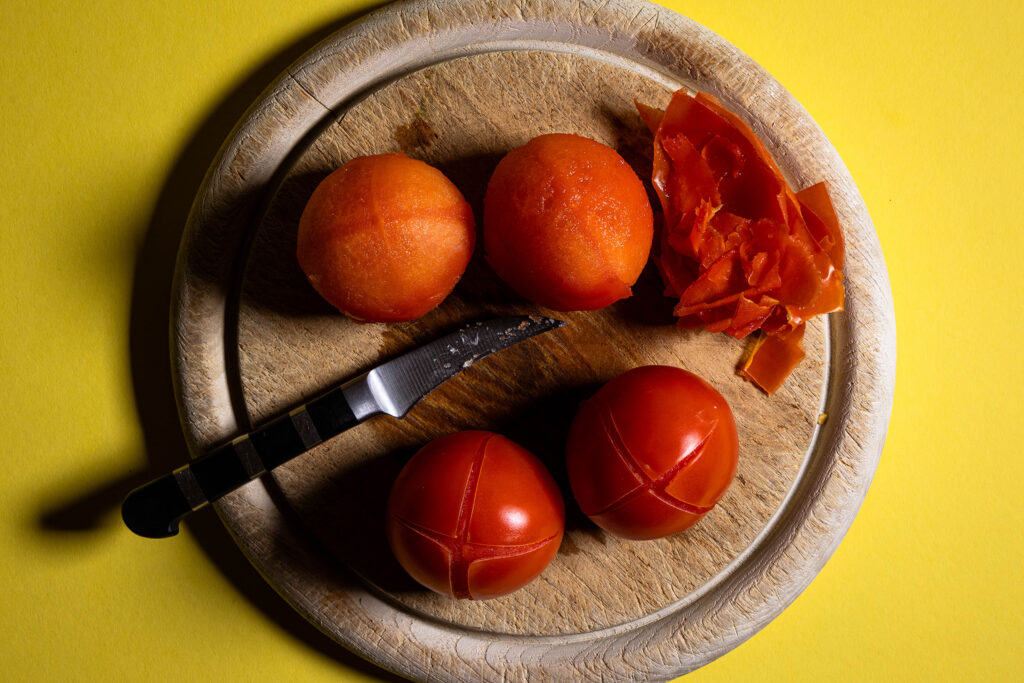 Blanschierte Tomaten werden auf einem Holzbrett gepellt.