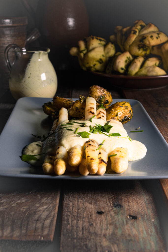 Weißer Spargel, hier gegrillt, mit meiner veganen Sauce Hollandaise und Ofenkartoffeln, die ich nach dem Backen in Bärlauchpesto geschwenkt habe. Im Hinterfgrund Bärlauch-Zupfbrote.
