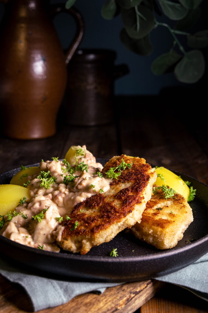 Sellerieschnitzel, Kartoffeln und vegane Schinken-Pilz-Sauce auf einem Teller.