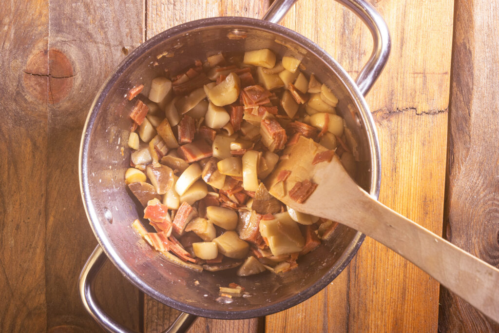 Kräuterseitlinge und veganer Schinken braten in einem Topf.