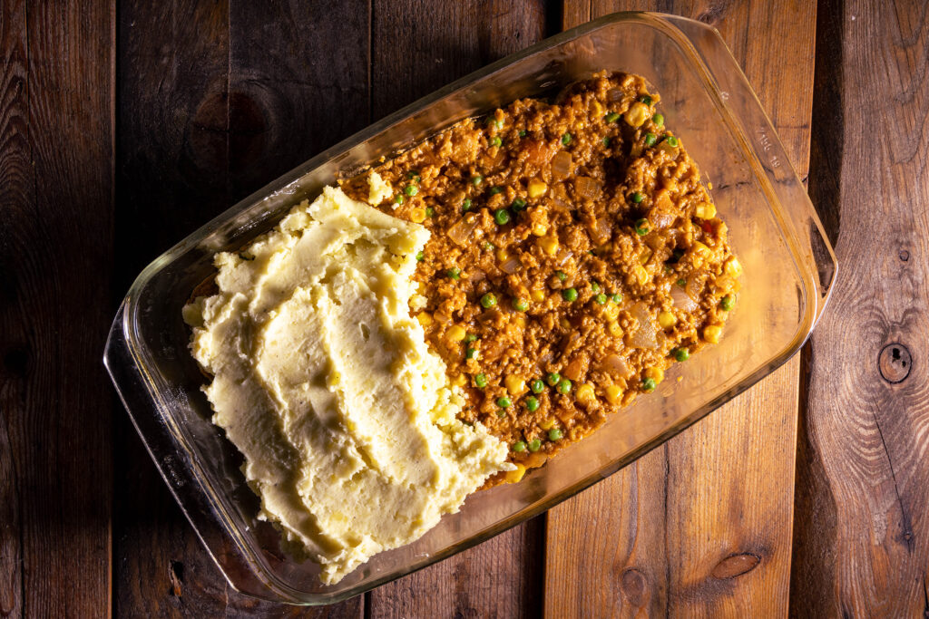 Eine vegane Fleischfüllung in einer Auflaufform wird mit Kartoffelpüree bedeckt.