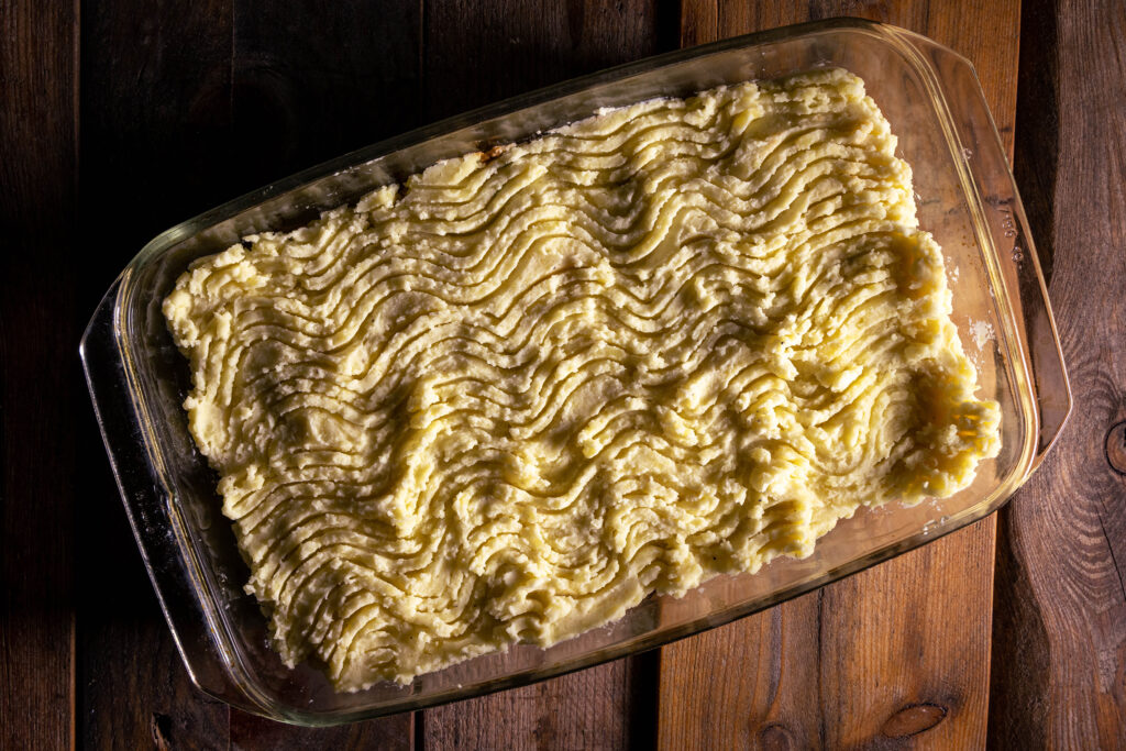Ein roher, veganer Sheperd's Pie, bereit für den Ofen. Man sieht das typische Wellenmuster in der Kartoffebreidecke.