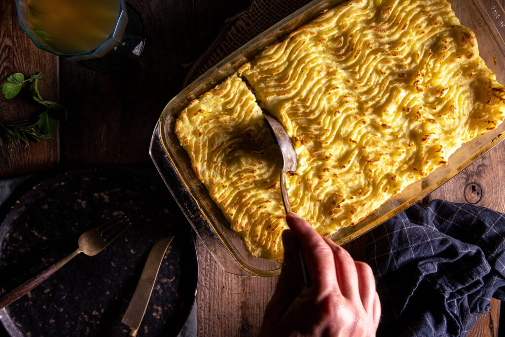 Ein verganer Sheperd's Pie mit Kartoffelbreikruste. Ein Löffel stih die Kruste an.
