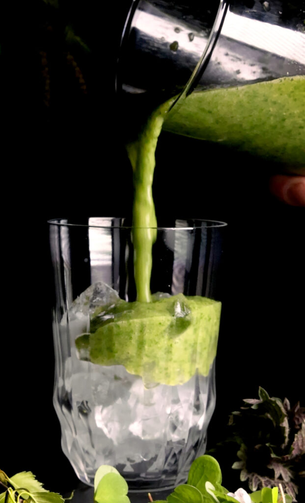 Wildkräuter-Smoothie aus jungen Birkenblättern, Sauerklee und Brennnessel wird in ein Glas gegossen.
