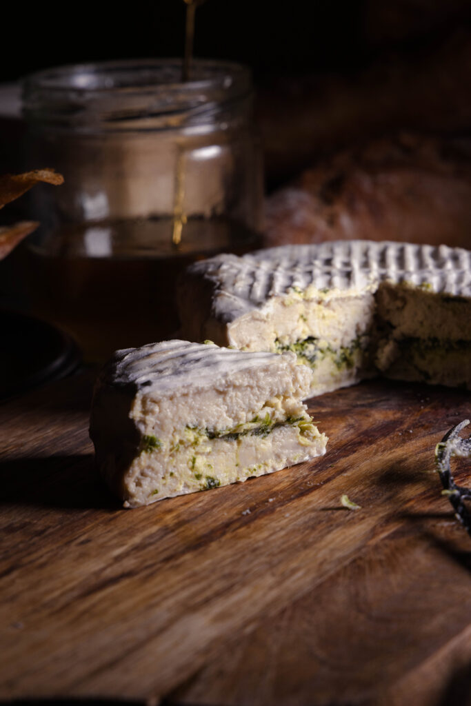 Mit Bärlauch durchzogener veganer Camembert angeschnitten auf einem Holzbrett.