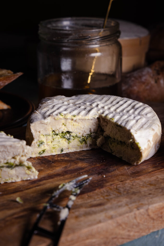Veganer Bärlauch-Camembert auf einem Holzbrett, angeschnitten.