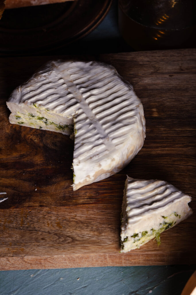 Veganer Bärlauch-Camembert auf einem Holzbrett, angeschnitten.