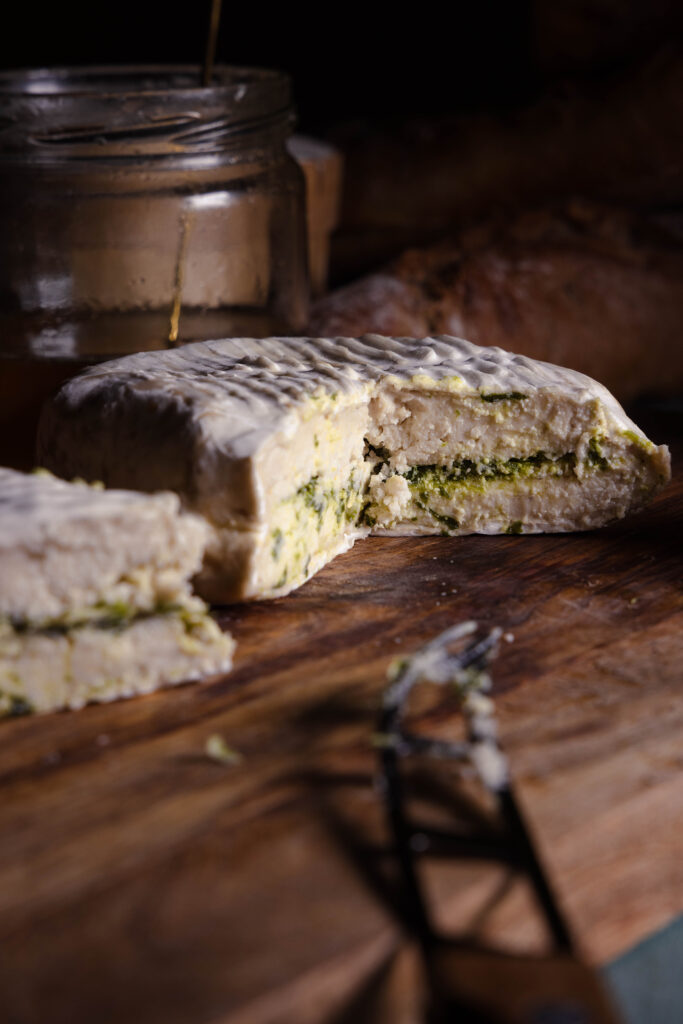 Veganer Bärlauch-Camembert auf einem Holzbrett, angeschnitten.