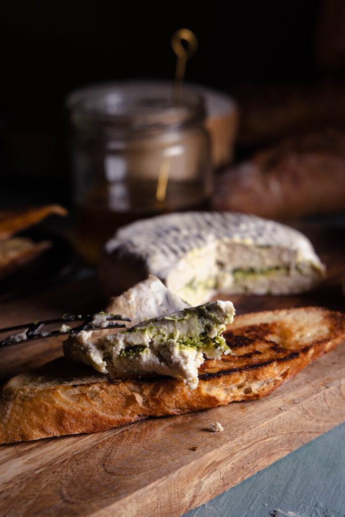 Mit Bärlauch durchzogener veganer Camembert wird auf ein geröstetes Brot gegeben