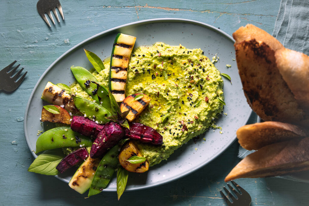 Grüner Umami-Dip aus Erbse und fermentiertem Brokkoli mit Grillgemüse auf einem grünen Teller.
