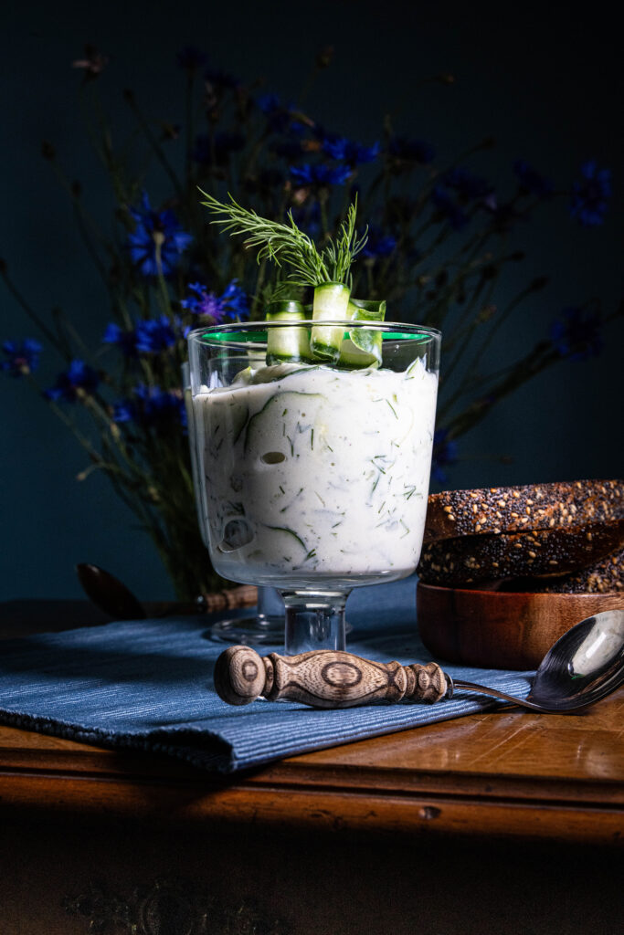 Gurkensuppe - vegan - in zwei Gläsern auf einem alten Holztisch, dahinter Kornblumen