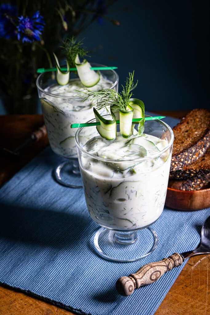 Gurkensuppe - vegan - in zwei Gläsern auf einem alten Holztisch, dahinter Kornblumen